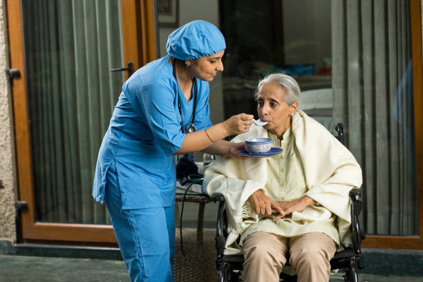 female caregiver feeding food to disabled senior woman on wheelchair